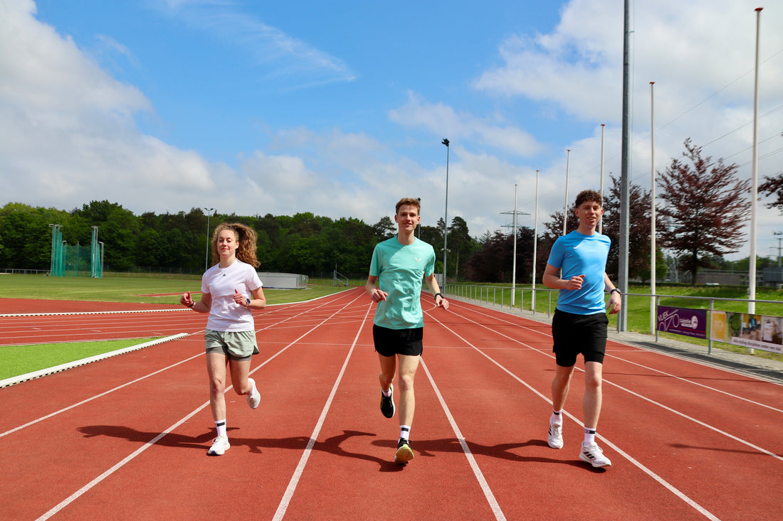 3 personen die aan het hardlopen zijn op een atletiekbaan.